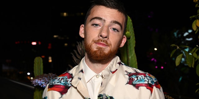 Angus Cloud in a patterned jacket looks at the camera