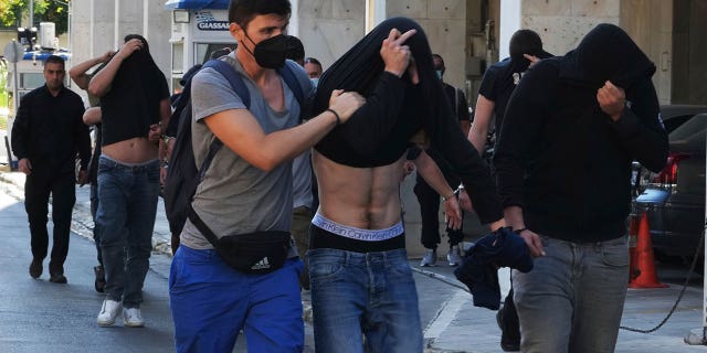 men cover their faces during police escort