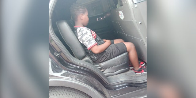 Boy shown in back of squad car.