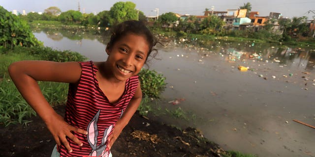 girl smiles near Brazilian river covered in litter