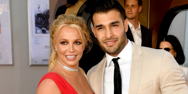 Britney Spears in a red dress and Sam Asghari in an off-white/tan suit and black tie