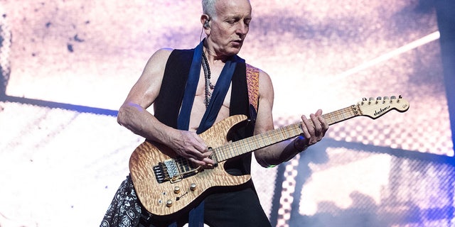 Phil Collen performs in Denmark, playing the electric guitar wearing an open vest, no shirt underneath and a loose navy tie