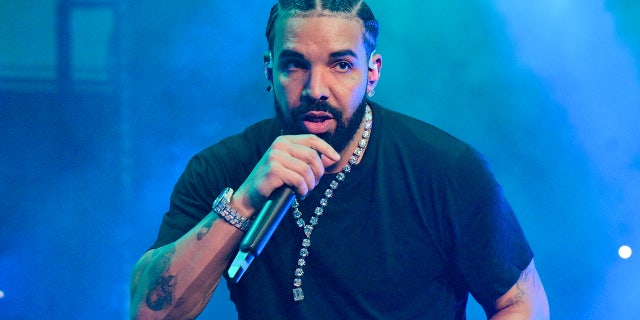 Drake in a black shirt and long chain raps into a microphone while onstage in Atlanta