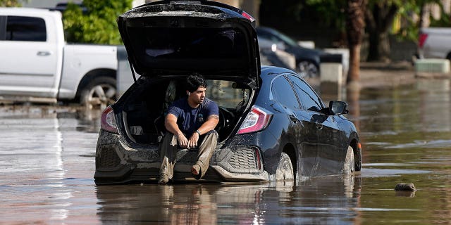 man waits in car stuck in flooded street