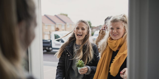 Two women greeted at a door by host.