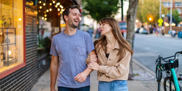 Couple with a visible height difference walks arm-in-arm down street.