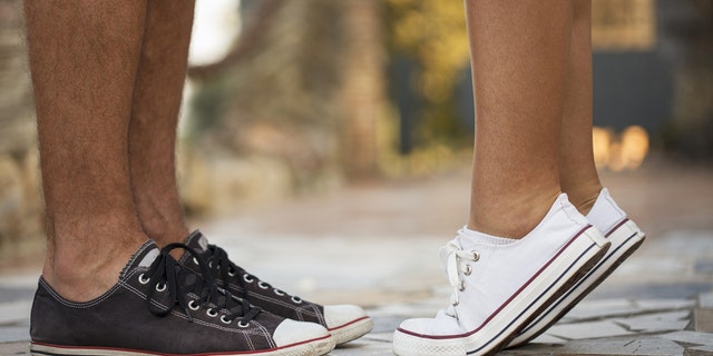 Close-up view of sneakers in which it appears a girl is getting on her tip toes to kiss a boy.