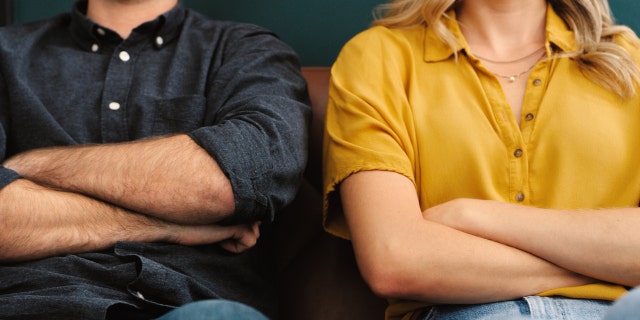 Upset couple sit next to each other and cross arms.
