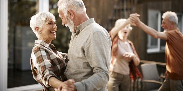 Two senior couples with height differences dance at a gathering.