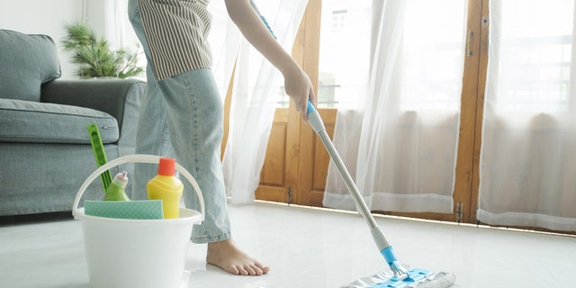 Woman mops floors with bucket nearby.