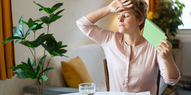 Woman fans herself with pills and glass of water in front of her.