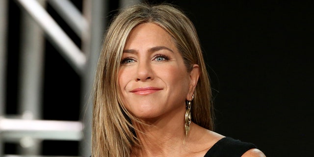 Jennifer Aniston in a black dress soft smiles on stage