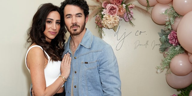 Danielle Jonas in a white tank top places her hand on her husband Kevin Jonas' chest, he's wearing a jean jacket at a boutique
