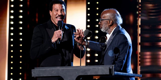 Lionel Richie holds a microphone as he presents Clarence Avant with an award at the Rock & Roll Hall of Fame induction