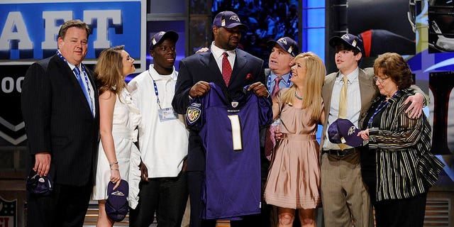 Michael Oher holds a Baltimore Ravens jersey on stage and poses with his family including the Tuohy's on stage
