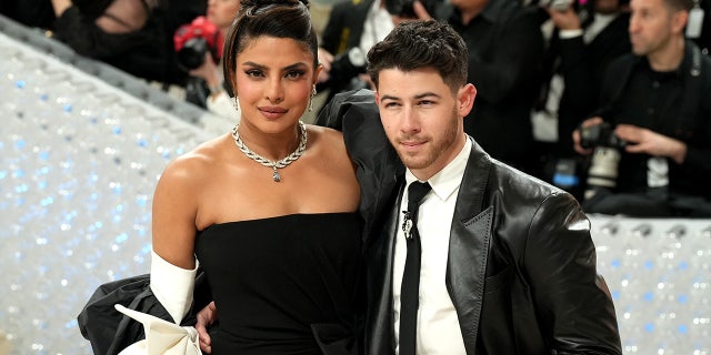 Priyanka Chopra in a black gown and updo smiles on the Met Gala carpet with husband Nick Jonas in a leather black suit