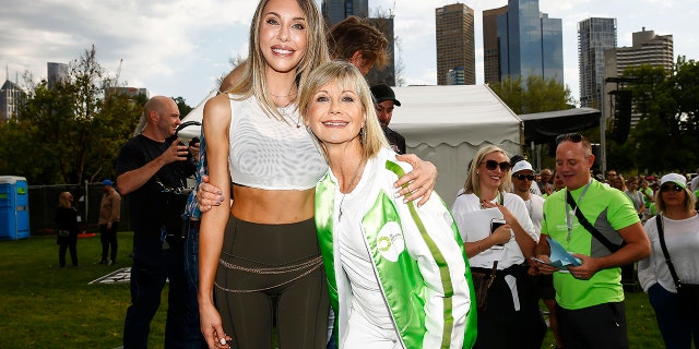 Chloe Lattanzi in a crop top and leggings holds on to her mother Olivia Newton-John in a white and green jacket at the Olivia Newton-John Wellness Walk and Research run in 2019