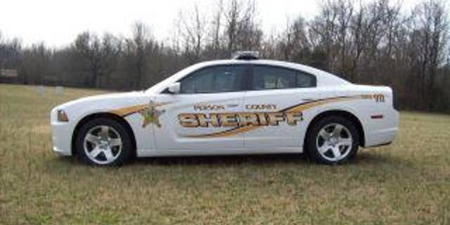 Police car in grass, woods behind it