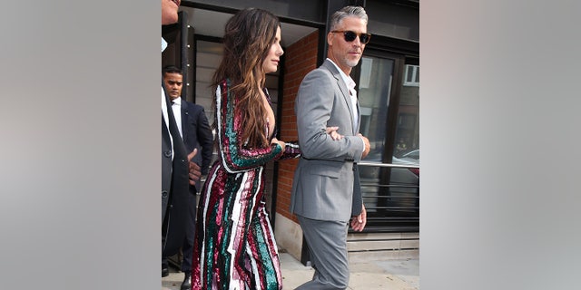 Sandra Bullock in multi-colored striped dress holds onto the arm of Bryan Randall in a grey suit