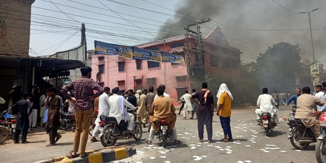 People stand on the street and watch as smoke rises from a burning church in Pakistan