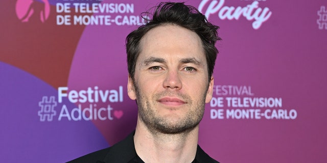 Taylor Kitsch tilts his head up a little and soft smiles wearing black in Monte-Carlo