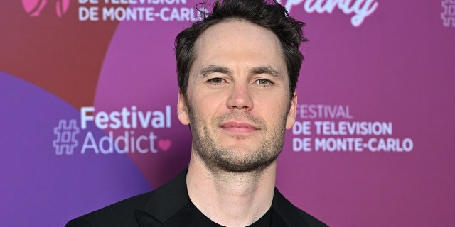 Taylor Kitsch tilts his head up a little and soft smiles wearing black in Monte-Carlo