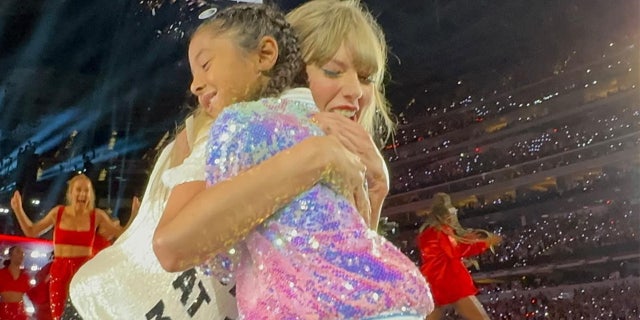 Taylor Swift in her 'Red' era hugs little Bianka Bryant at the end of the stage wearing a purple tutu and multi-colored sequin jacket