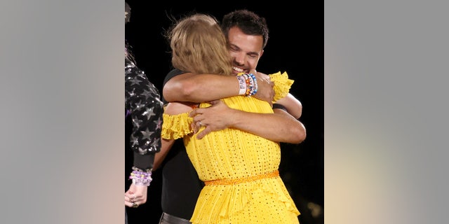 Taylor Swift in a yellow dress gives a beaming Taylor Lautner a hug on stage