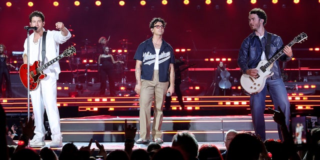 Nick in all white, Joe Jonas in a jersey and Kevin in a blue jacket perform at Yankee Stadium for opening night of "The Tour"
