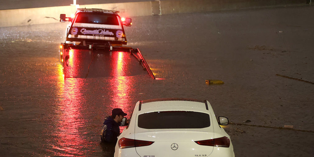 Tow truck driver attempts to pull a stranded car out of floodwaters