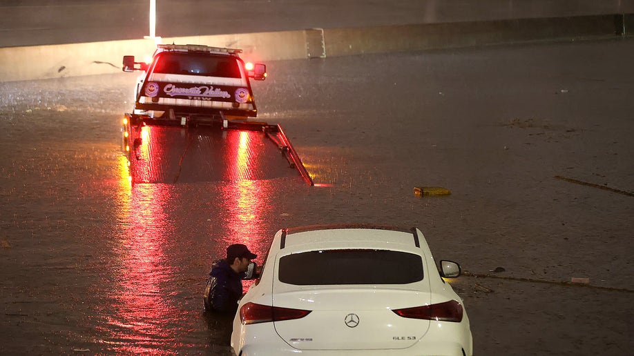 tow truck driver attempts to pull a stranded car out of floodwaters