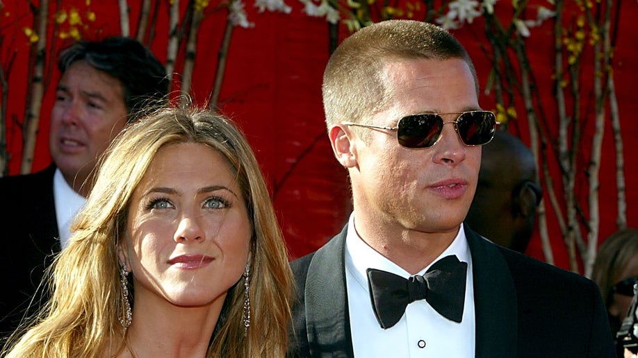 Jennifer Aniston looks off in the distance at the Emmy Awards carpet while Brad Pitt wheres a tuxedo and sunglasses