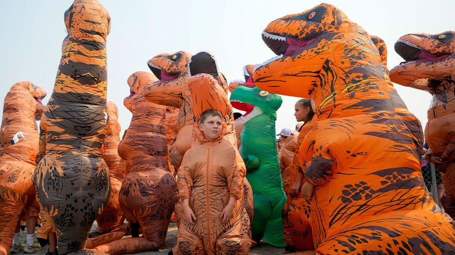 People in inflatable T. rex costumes queue in line