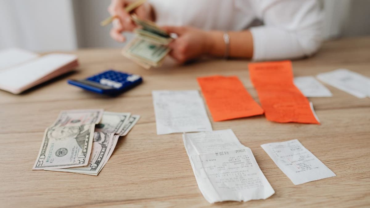 Person counting money on table with calculator, pencil and notes
