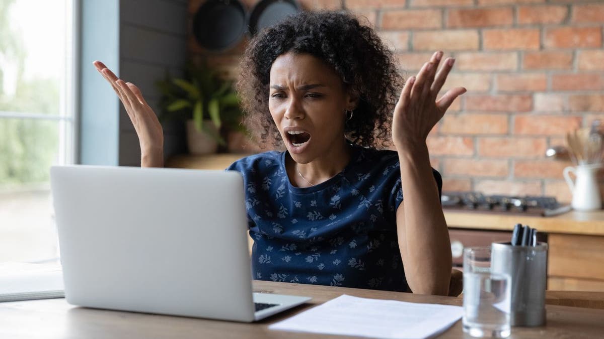 Woman looking at her laptop with a shocked face and her hands in the air.