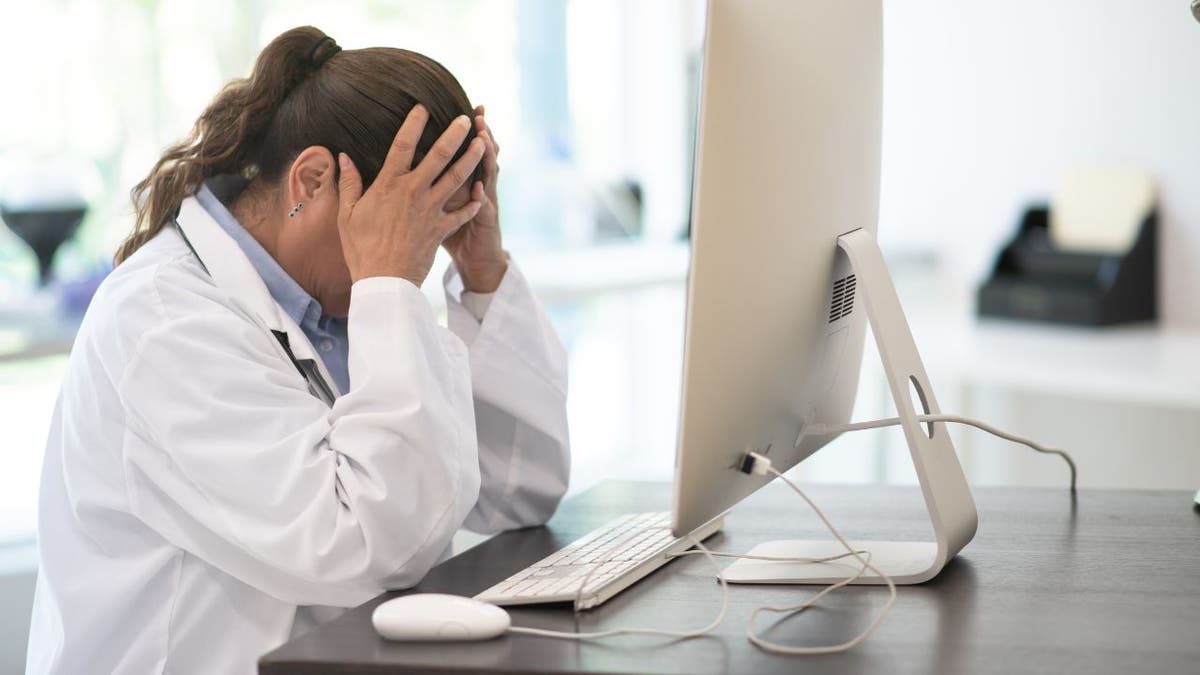 Woman sitting at her desk, in front of her computer with her hands on her head.