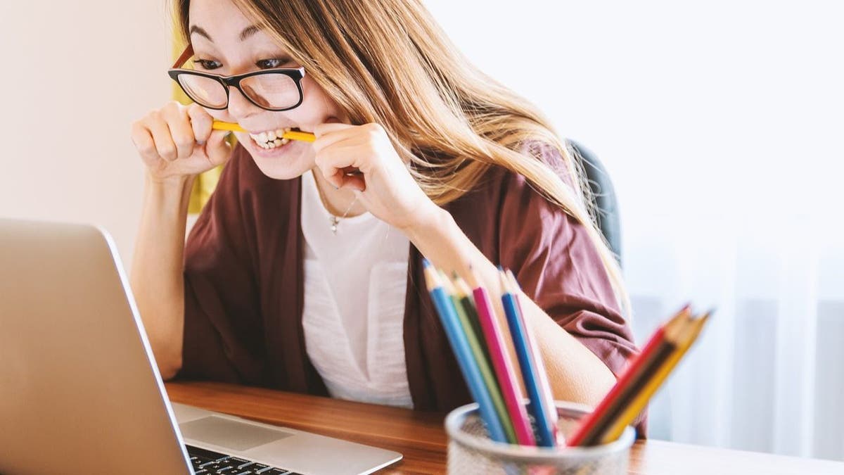 Woman looking at her laptop and biting her pencil.