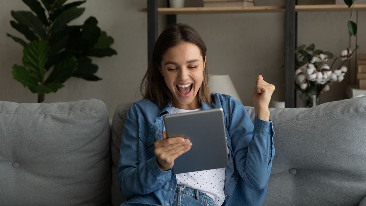 Woman smiling at her tablet with a celebratory fist in the air.