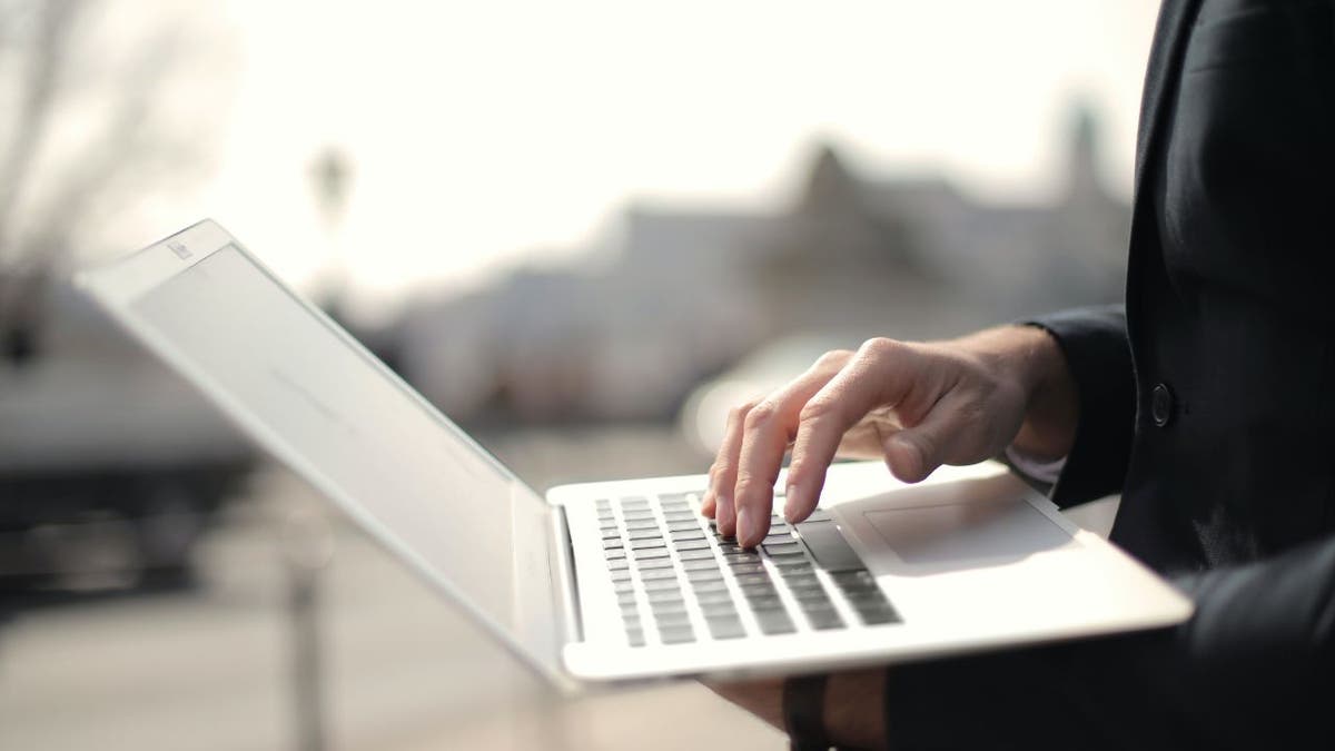 Woman holding up her laptop with one hand while typing with the other.