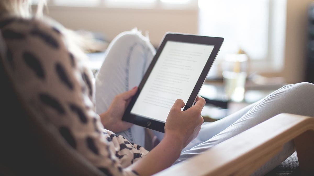 Woman sitting criss-cross in a chair while reading on an Amazon Kindle