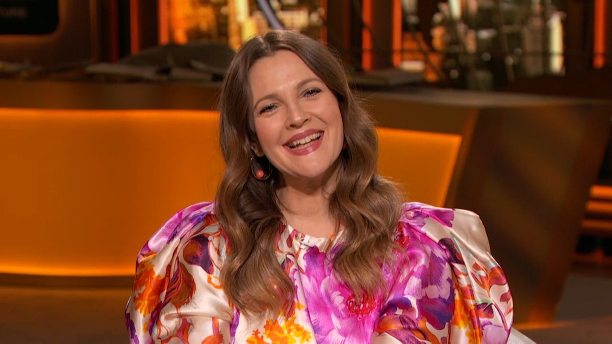 Drew Barrymore in a colorful printed dress tilts her head and smiles for the camera