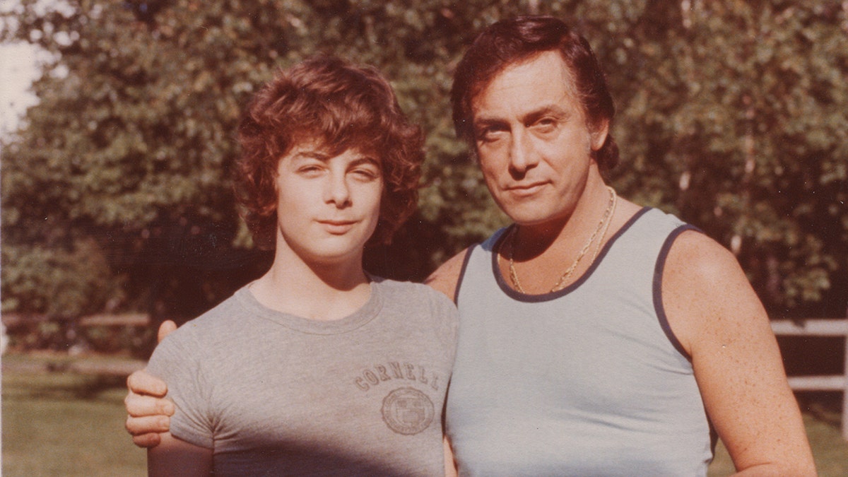 A young Nicholas Guccione in a grey t-shirt being embrace by his father in a grey tank top