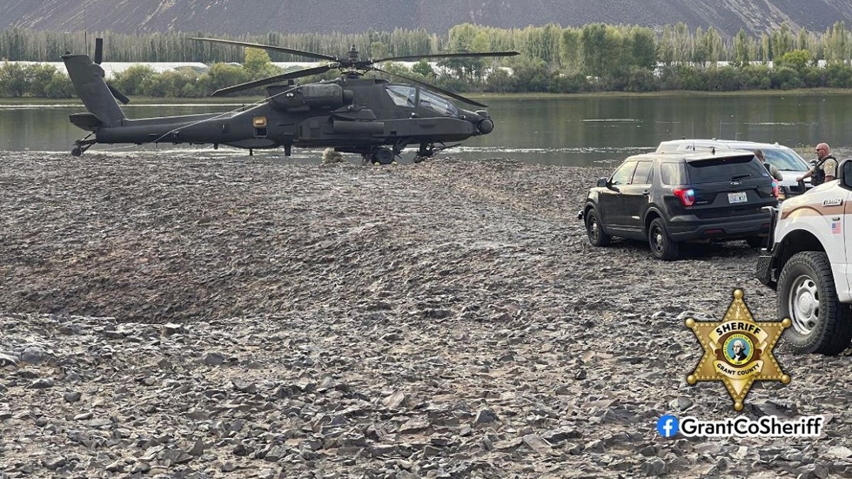 An Army helicopter landing near a river and Grant County sheriff's vehicles