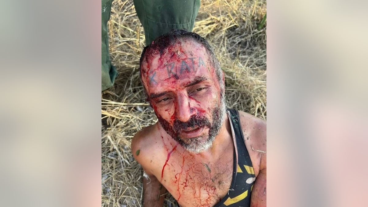 A suspected migrant smuggler sits bloodied with the word "rata," meaning rat, tattooed on his forehead