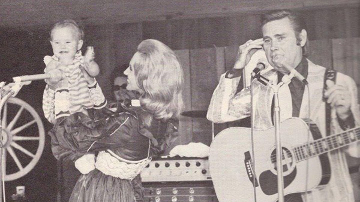 Tammy Wynette holding Georgette Jones as George Jones holds a guitar on stage