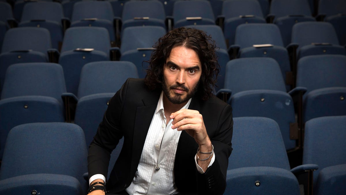 Russell Brand sitting in a chair