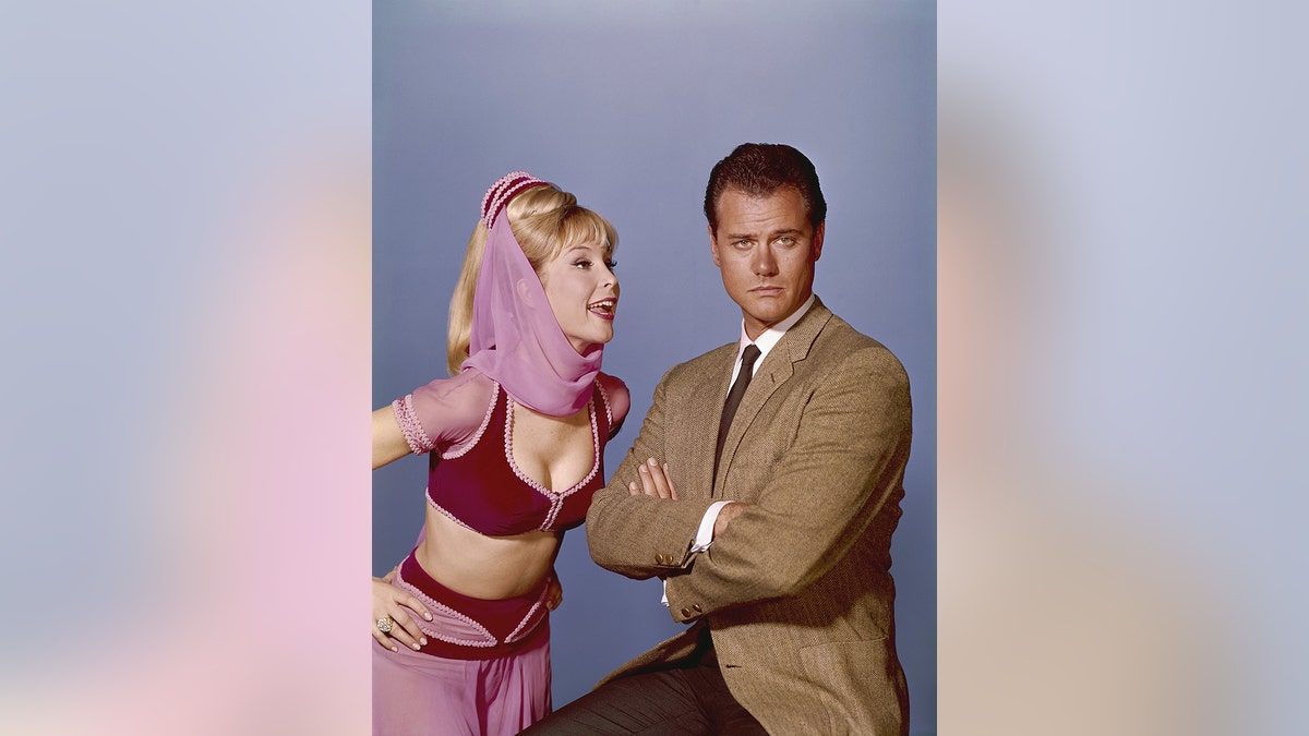 Barbara Eden in a genie costme poking fun at a serious looking Larry Hagman