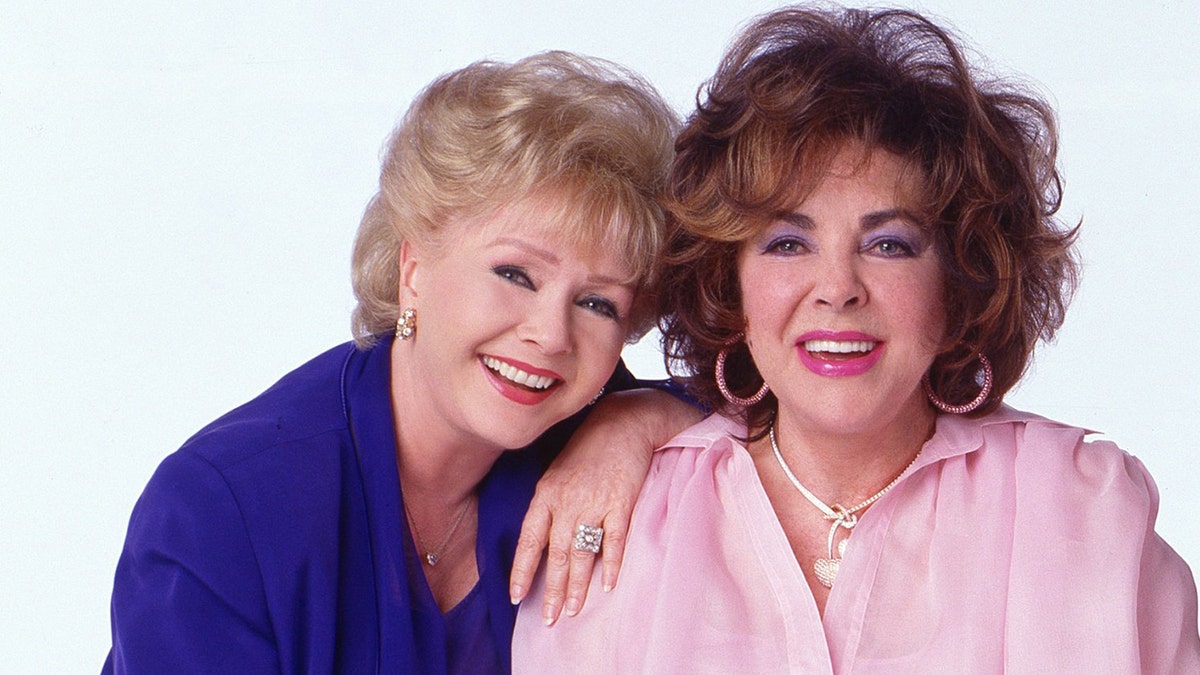 Debbie Reynolds wearing a blue suit and Elizabeth Taylor wearing a pink suit