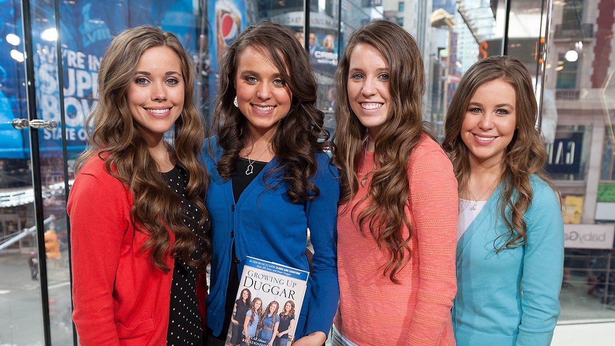 The Duggar sisters posing together and smiling in bright cardigans