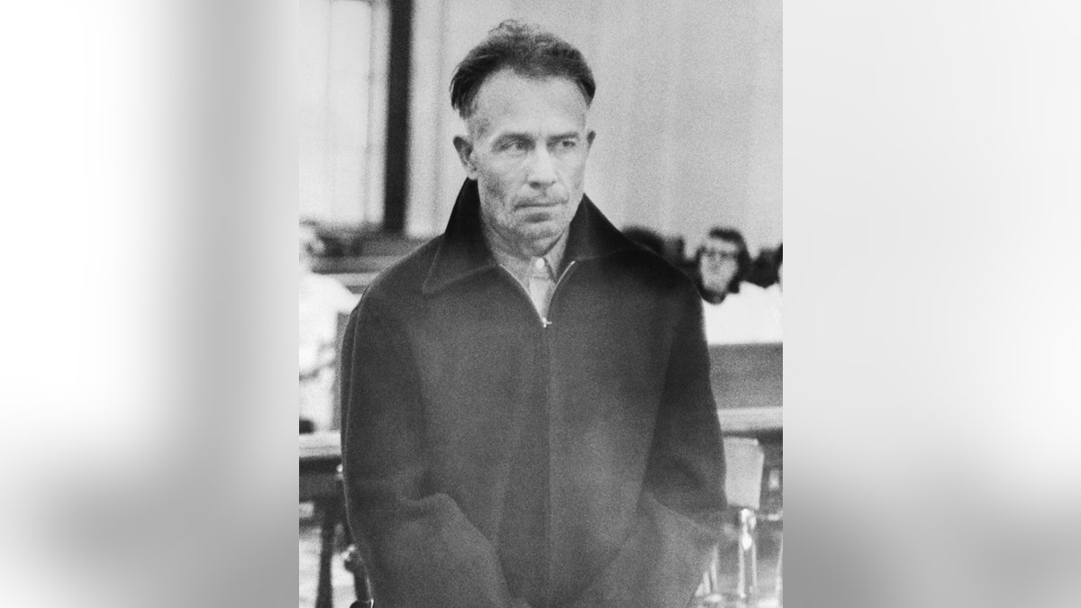A close-up of Ed Gein looking serious in a dark jacket